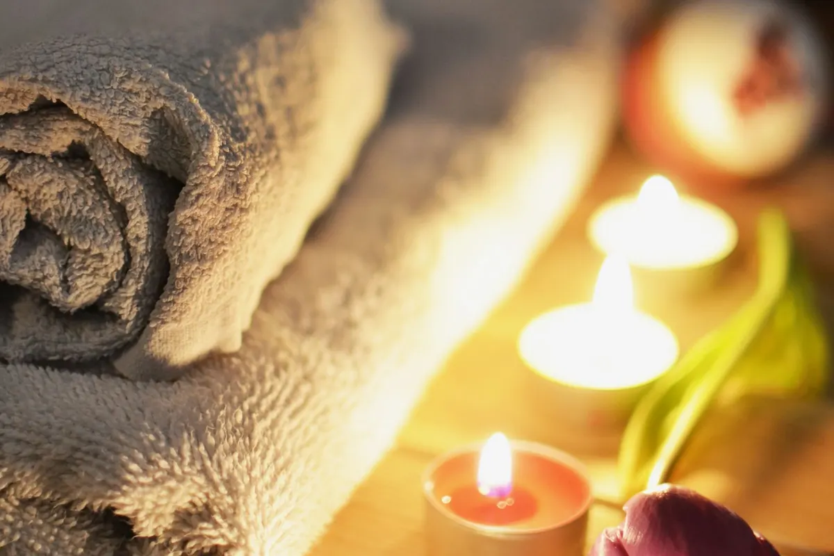 Lit candles, rolled towels and a flower set up for a calm home spa session