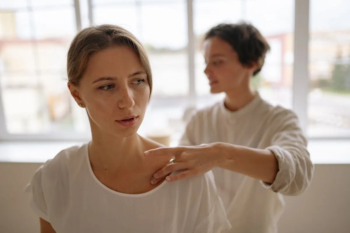 Therapist massaging a relaxed client's shoulder in a bright room