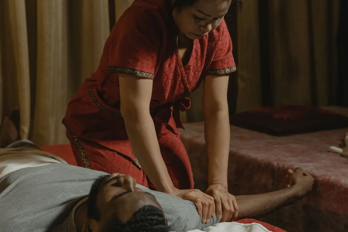 Therapist in a red uniform giving a fully clothed Thai massage on a floor mat